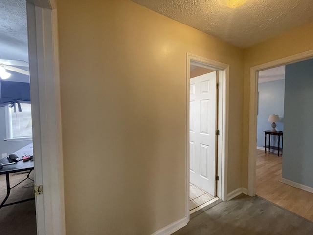 hall featuring a textured ceiling and baseboards