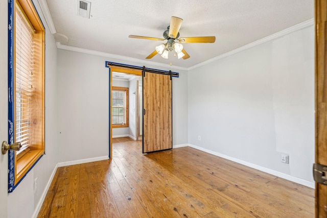 unfurnished room with hardwood / wood-style floors, crown molding, ceiling fan, a barn door, and a textured ceiling