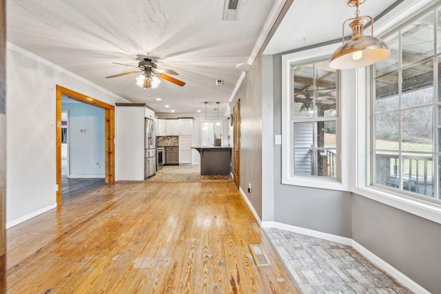 unfurnished living room featuring a textured ceiling, ceiling fan, light wood-type flooring, and crown molding