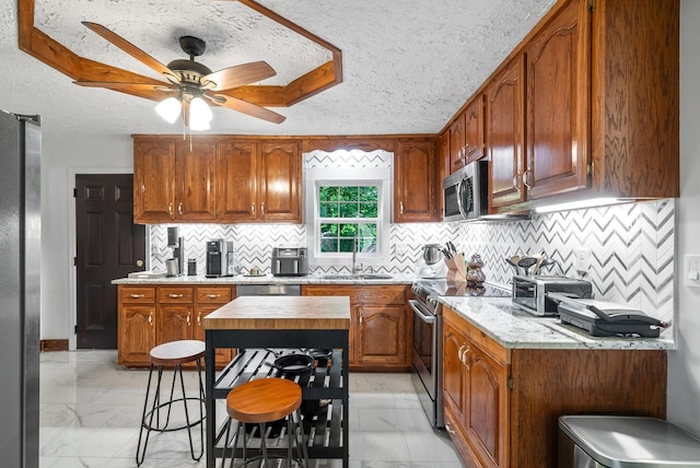 kitchen featuring a breakfast bar, sink, ceiling fan, a textured ceiling, and stainless steel appliances