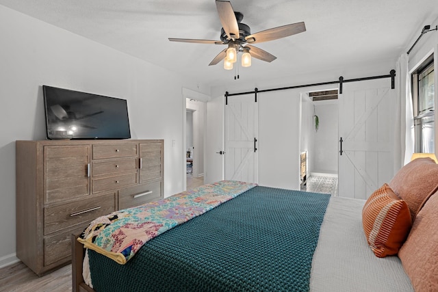 bedroom with a barn door, ceiling fan, and light wood-type flooring