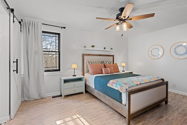 bedroom featuring a barn door, light hardwood / wood-style flooring, and ceiling fan