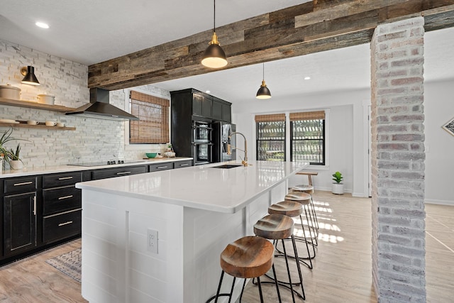 kitchen featuring a breakfast bar, a kitchen island with sink, sink, wall chimney range hood, and light hardwood / wood-style floors