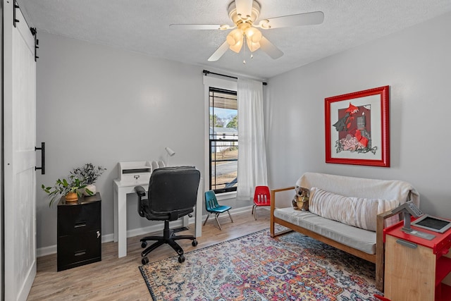 office featuring ceiling fan, a barn door, wood-type flooring, and a textured ceiling