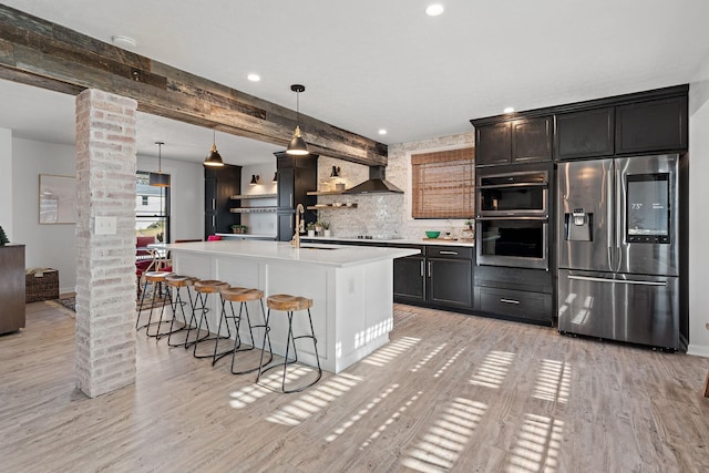 kitchen with pendant lighting, light hardwood / wood-style flooring, ornate columns, an island with sink, and appliances with stainless steel finishes