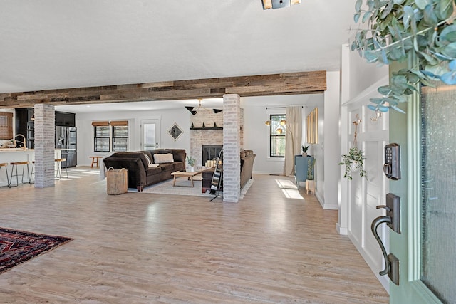 living room featuring beam ceiling, a brick fireplace, light hardwood / wood-style flooring, decorative columns, and a textured ceiling