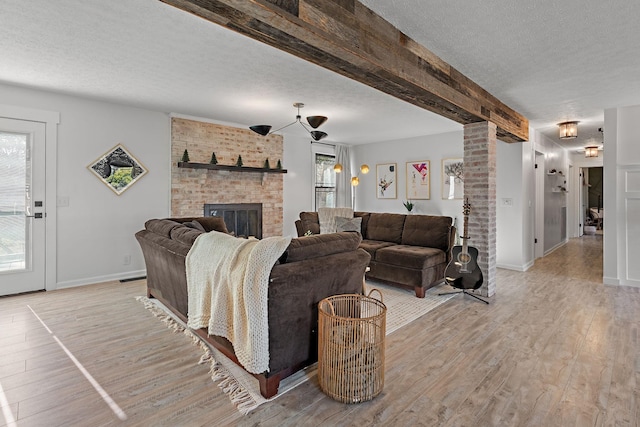 living room with beam ceiling, ornate columns, a textured ceiling, a fireplace, and light wood-type flooring