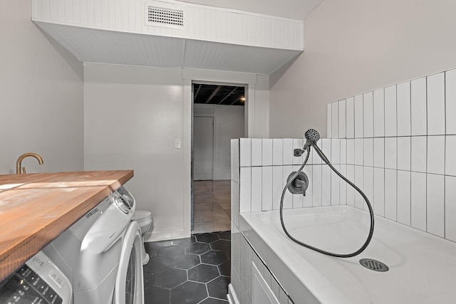 bathroom featuring tile patterned flooring, a bath, washer / clothes dryer, and toilet