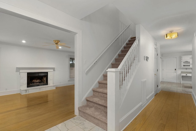 staircase with ceiling fan, wood-type flooring, and a fireplace