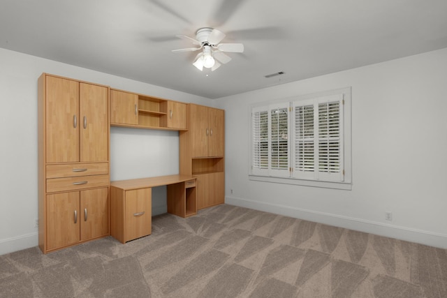 unfurnished office featuring built in desk, light colored carpet, and ceiling fan