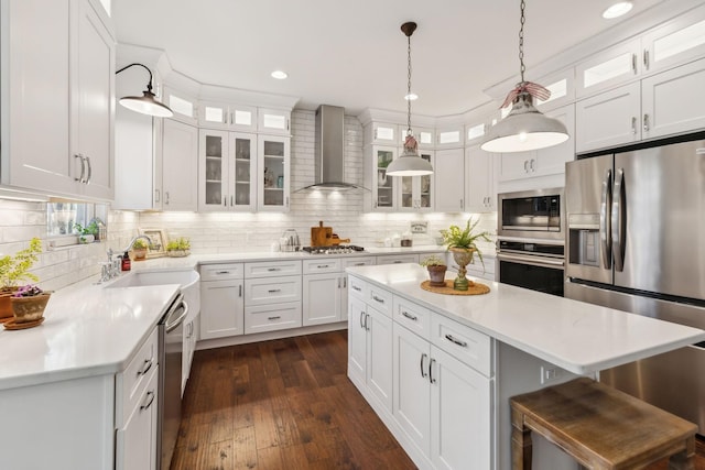 kitchen with appliances with stainless steel finishes, dark hardwood / wood-style flooring, wall chimney range hood, white cabinets, and hanging light fixtures