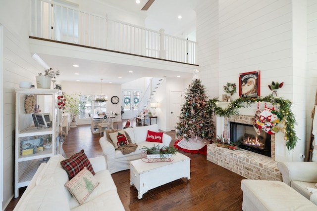 living room featuring ceiling fan, a towering ceiling, dark hardwood / wood-style floors, and a brick fireplace