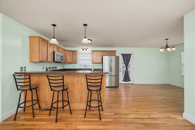 kitchen featuring kitchen peninsula, appliances with stainless steel finishes, light wood-type flooring, sink, and a notable chandelier