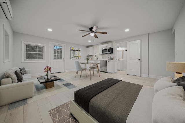 bedroom with a wall mounted AC, ceiling fan, light hardwood / wood-style flooring, and sink