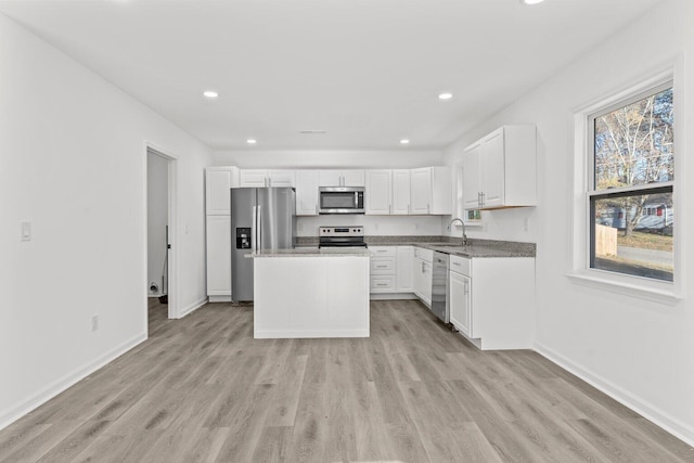 kitchen featuring stainless steel appliances, sink, a center island, light hardwood / wood-style floors, and white cabinetry