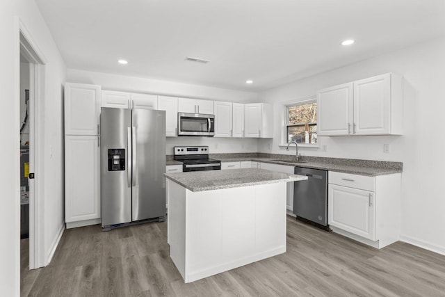 kitchen with sink, a kitchen island, appliances with stainless steel finishes, white cabinets, and light wood-type flooring