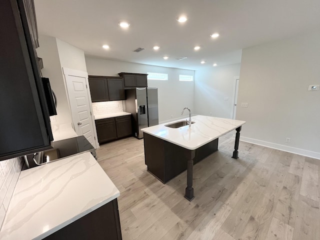 kitchen featuring stainless steel fridge with ice dispenser, sink, light hardwood / wood-style floors, and a center island with sink