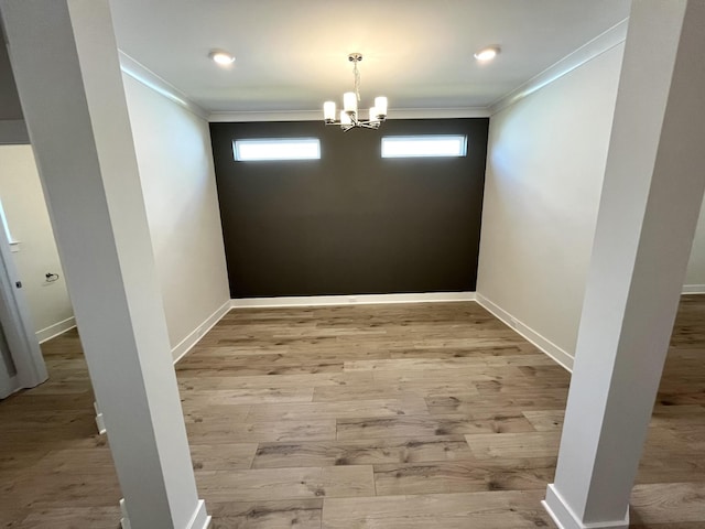 unfurnished dining area featuring crown molding, a notable chandelier, wood finished floors, and baseboards