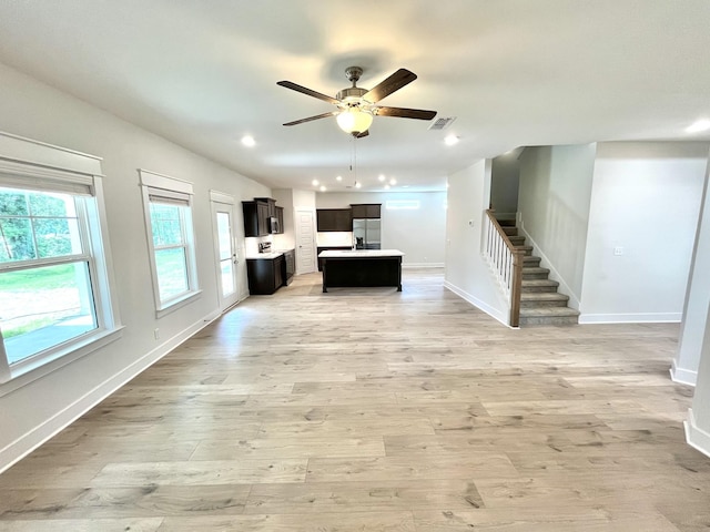 unfurnished living room with visible vents, baseboards, ceiling fan, light wood-type flooring, and stairs