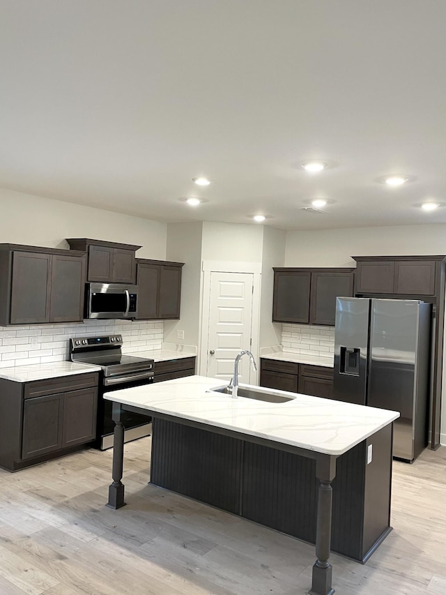 kitchen featuring a breakfast bar area, light stone counters, a sink, light wood-style floors, and appliances with stainless steel finishes