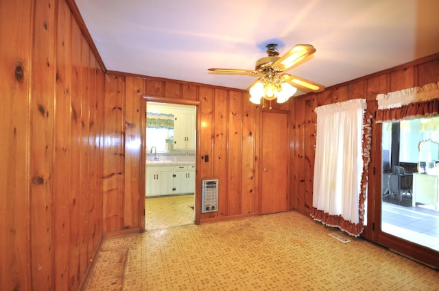 unfurnished room with crown molding, sink, wooden walls, ceiling fan, and heating unit