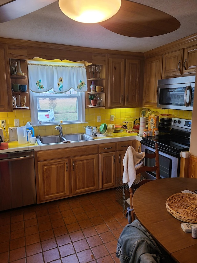 kitchen with sink, stainless steel appliances, tile patterned floors, tile countertops, and backsplash