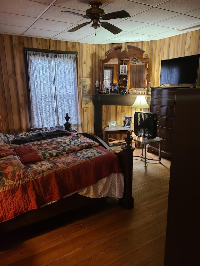 bedroom featuring a paneled ceiling, hardwood / wood-style flooring, ceiling fan, and wood walls