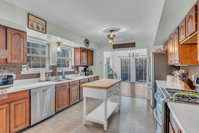 kitchen featuring tasteful backsplash, brown cabinetry, stainless steel appliances, light countertops, and a sink