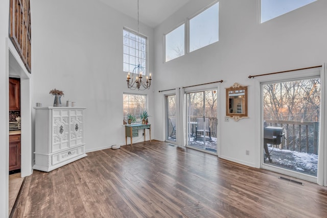 unfurnished living room with a notable chandelier, visible vents, a towering ceiling, wood finished floors, and baseboards