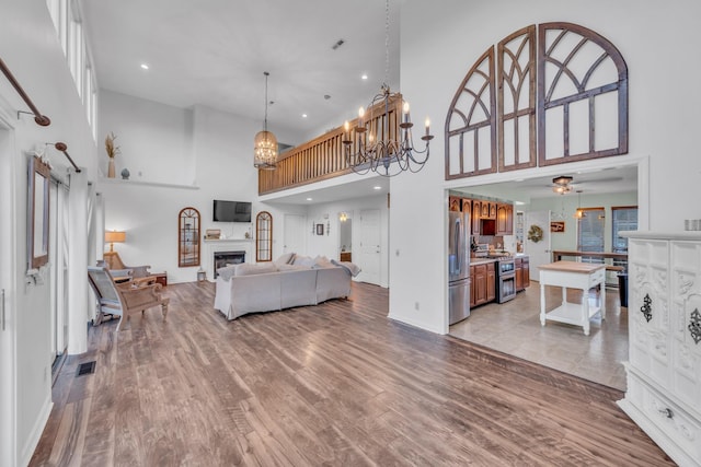 living area featuring light wood-style floors, a fireplace, a high ceiling, and ceiling fan with notable chandelier