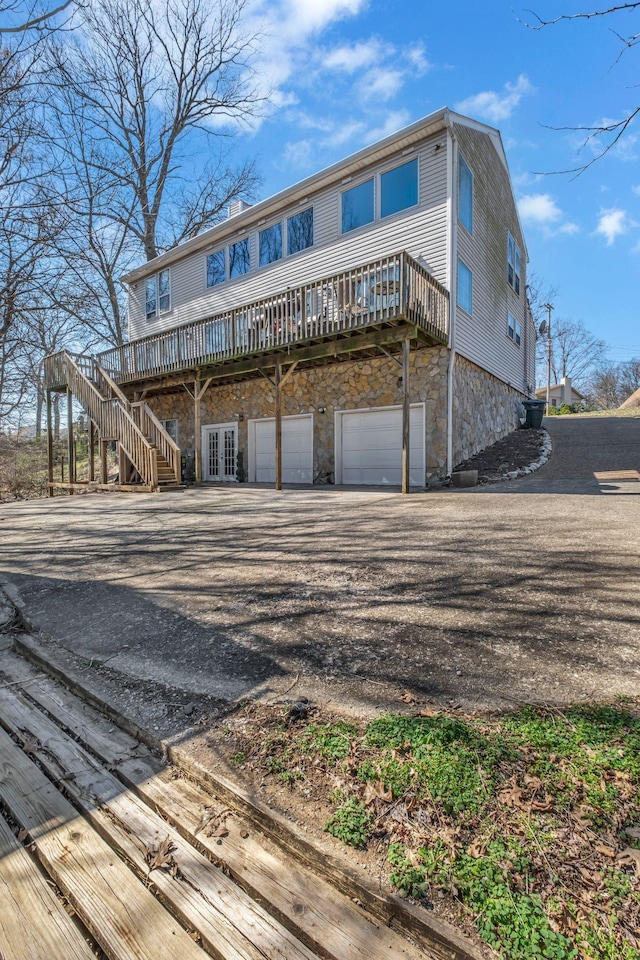 rear view of property featuring stone siding, french doors, driveway, and an attached garage