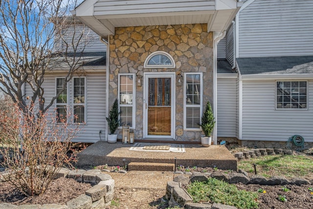 doorway to property with stone siding and a shingled roof