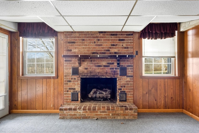 unfurnished living room with a drop ceiling, wood walls, and a fireplace