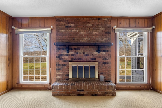 unfurnished living room with a wealth of natural light, light colored carpet, wood walls, and a brick fireplace