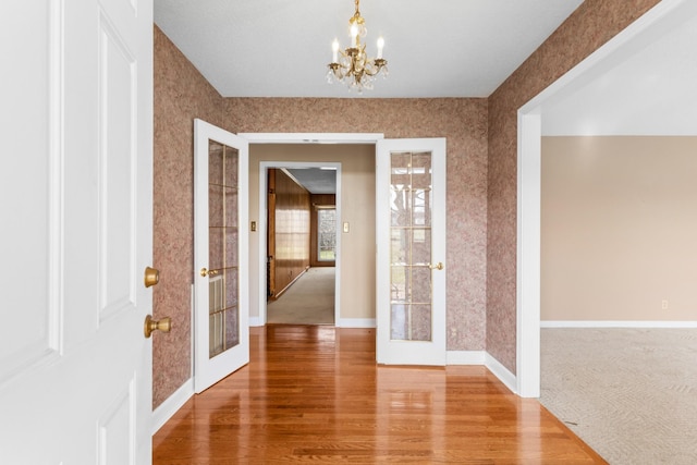 hall with french doors, a notable chandelier, and hardwood / wood-style floors