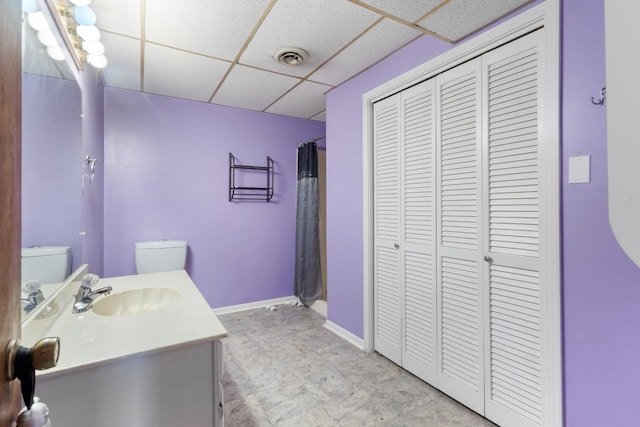 bathroom with walk in shower, a drop ceiling, vanity, and toilet