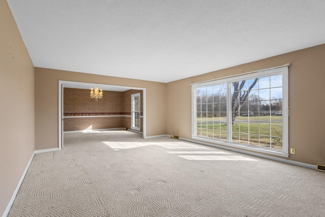 unfurnished room featuring a notable chandelier, light colored carpet, and a textured ceiling