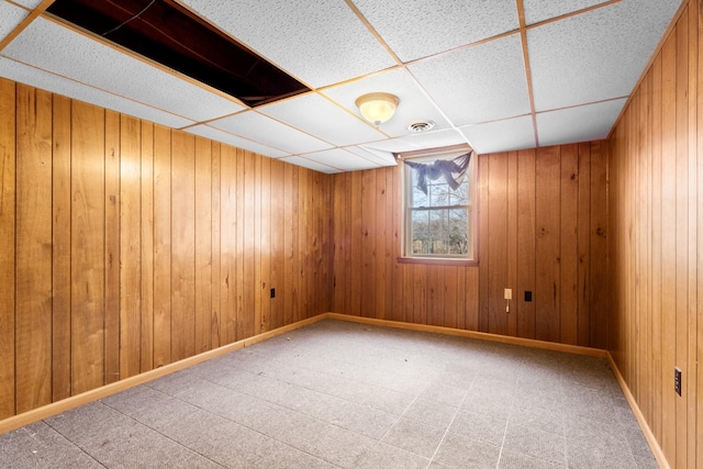 spare room with a drop ceiling and wood walls