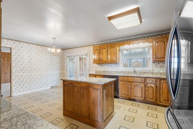 kitchen with sink, hanging light fixtures, light stone counters, a notable chandelier, and appliances with stainless steel finishes