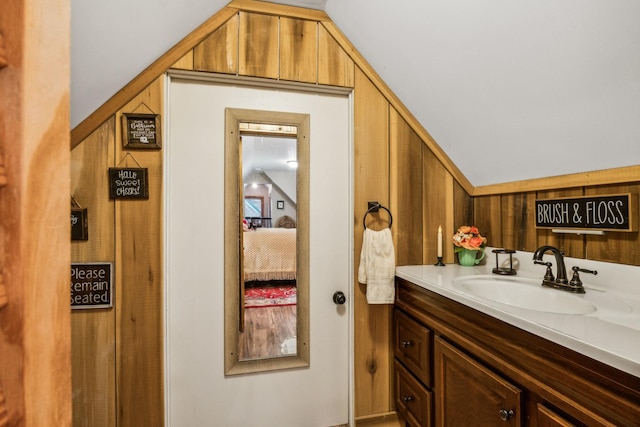 bathroom with vaulted ceiling, vanity, and wooden walls