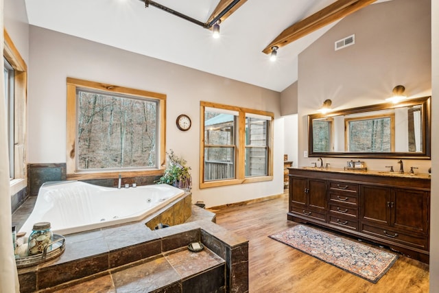 bathroom featuring beam ceiling, hardwood / wood-style flooring, a bathtub, and a healthy amount of sunlight