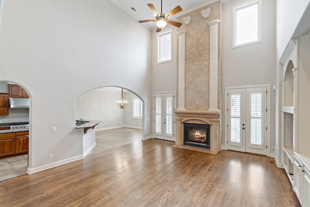 unfurnished living room featuring ceiling fan with notable chandelier, a healthy amount of sunlight, a premium fireplace, and crown molding