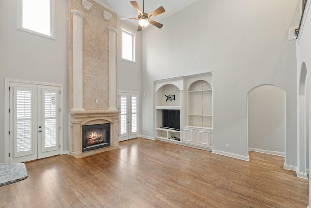 unfurnished living room featuring built in shelves, ceiling fan, french doors, a premium fireplace, and a towering ceiling