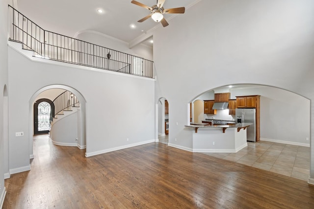 unfurnished living room with hardwood / wood-style floors, a towering ceiling, ceiling fan, and crown molding