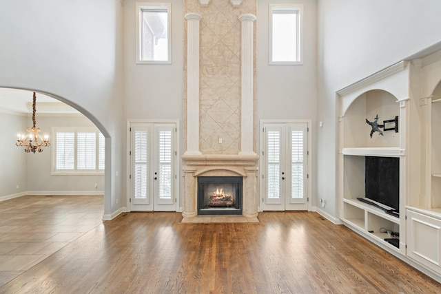 unfurnished living room featuring a notable chandelier, built in features, a wealth of natural light, and french doors