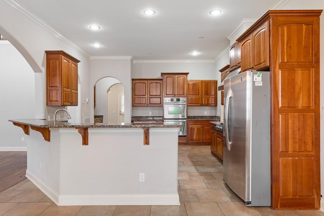 kitchen with a kitchen bar, appliances with stainless steel finishes, ornamental molding, and dark stone counters