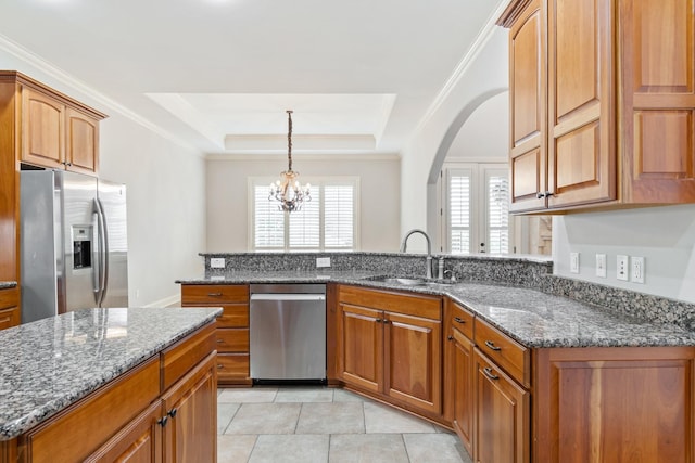 kitchen with appliances with stainless steel finishes, a tray ceiling, sink, an inviting chandelier, and dark stone countertops