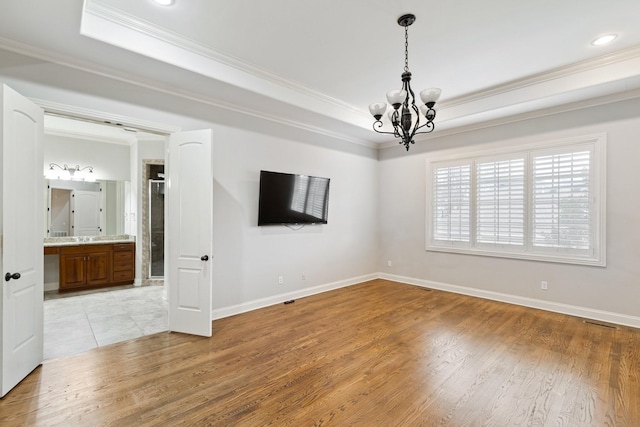 unfurnished room with a notable chandelier, crown molding, a tray ceiling, and light hardwood / wood-style flooring