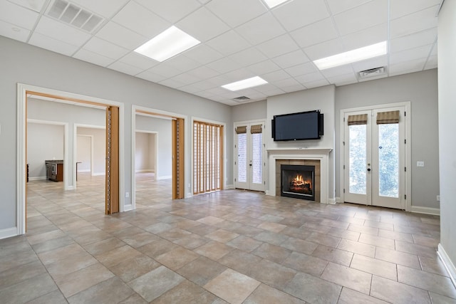 unfurnished living room featuring a paneled ceiling, french doors, and a tiled fireplace