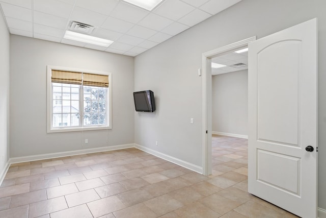 tiled empty room featuring a drop ceiling